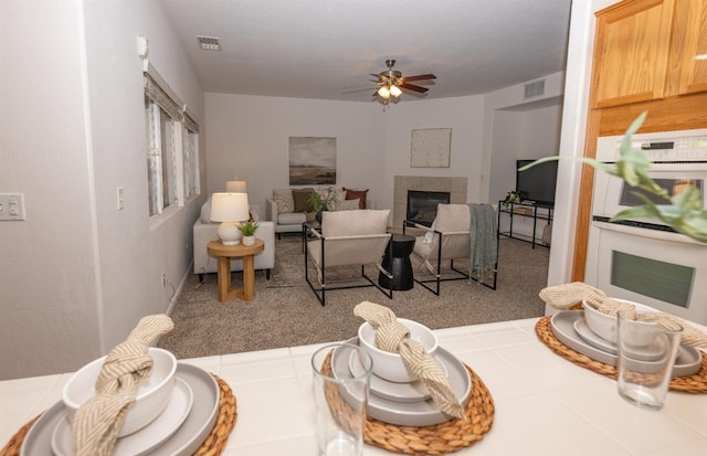 living room featuring light carpet, a tile fireplace, and ceiling fan