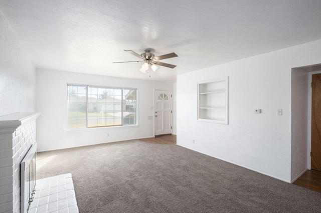 unfurnished living room with a brick fireplace, carpet floors, built in features, and ceiling fan