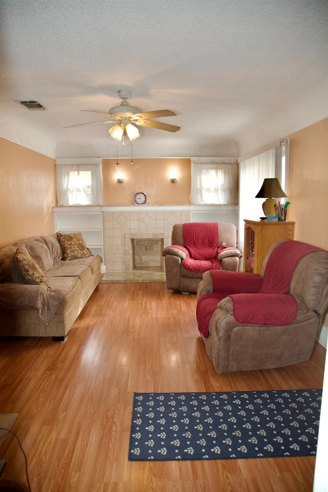 living area with a textured ceiling, ceiling fan, a tile fireplace, visible vents, and light wood-type flooring