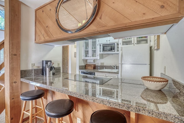 kitchen with sink, white refrigerator, stainless steel microwave, black electric stovetop, and a kitchen bar