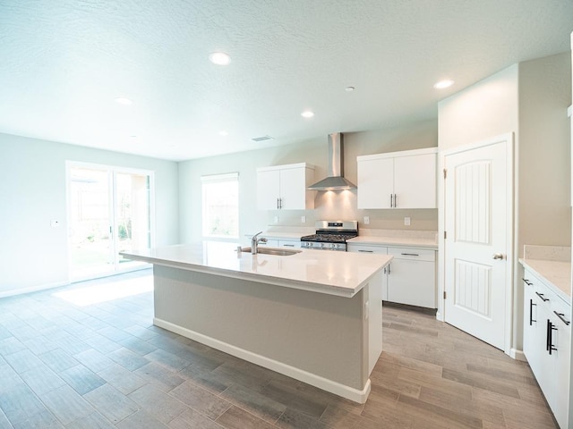 kitchen featuring white cabinetry, wall chimney exhaust hood, an island with sink, and stainless steel gas stove