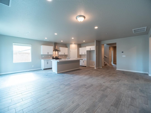 kitchen with white cabinetry, light hardwood / wood-style flooring, stainless steel electric range, a center island with sink, and wall chimney range hood