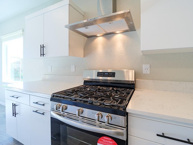 kitchen featuring white cabinets, stainless steel range with gas cooktop, light stone countertops, and wall chimney range hood