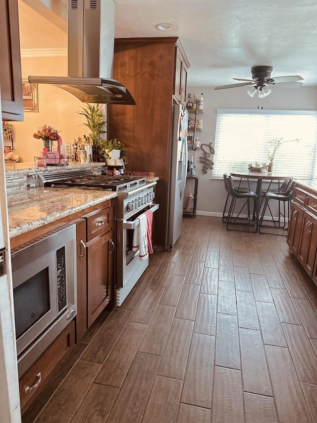 kitchen featuring appliances with stainless steel finishes, island range hood, light stone countertops, and ceiling fan