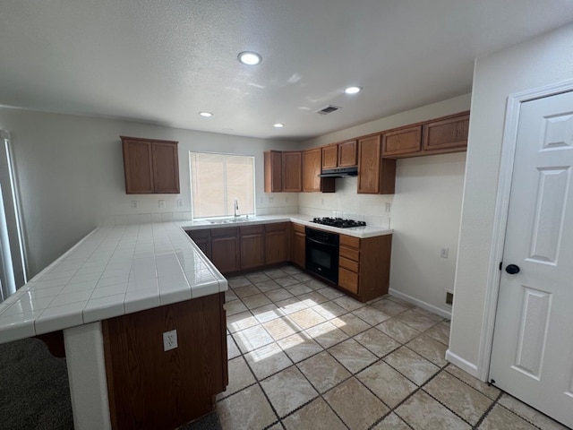 kitchen featuring sink, tile countertops, black appliances, and kitchen peninsula