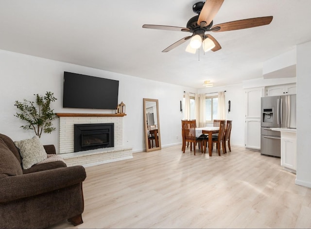 living room with a brick fireplace, ceiling fan, and light wood-type flooring