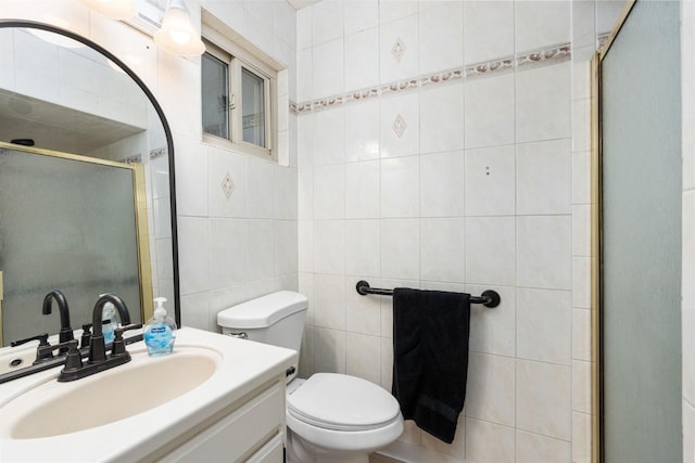 bathroom with vanity, toilet, a shower with door, and tile walls