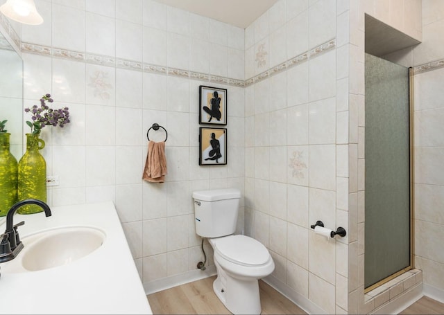 bathroom featuring sink, hardwood / wood-style flooring, a shower with door, tile walls, and toilet