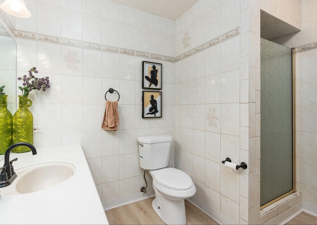 bathroom featuring wood finished floors, a stall shower, toilet, tile walls, and vanity