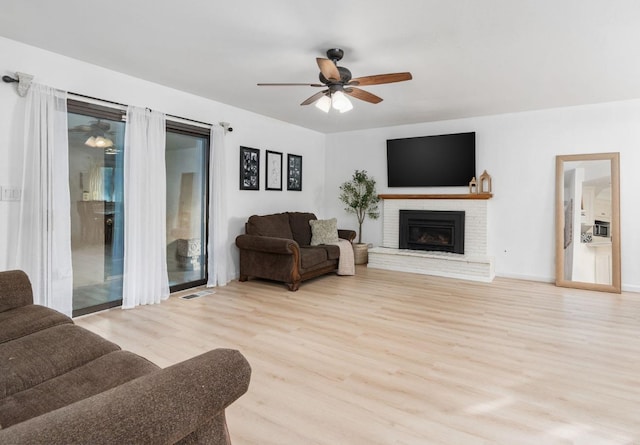 living room featuring ceiling fan, light hardwood / wood-style floors, and a brick fireplace