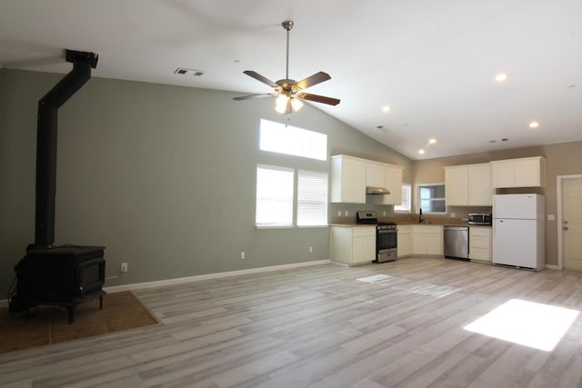 kitchen featuring light wood finished floors, visible vents, appliances with stainless steel finishes, a wood stove, and under cabinet range hood