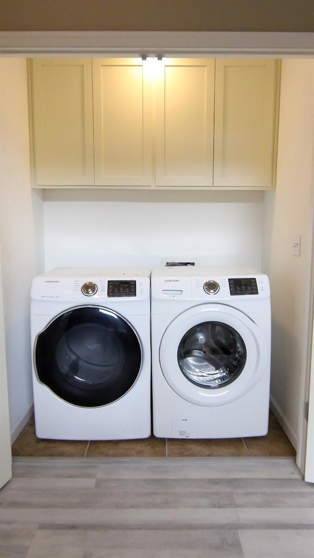 laundry area featuring baseboards, washing machine and dryer, cabinet space, and light wood-style floors