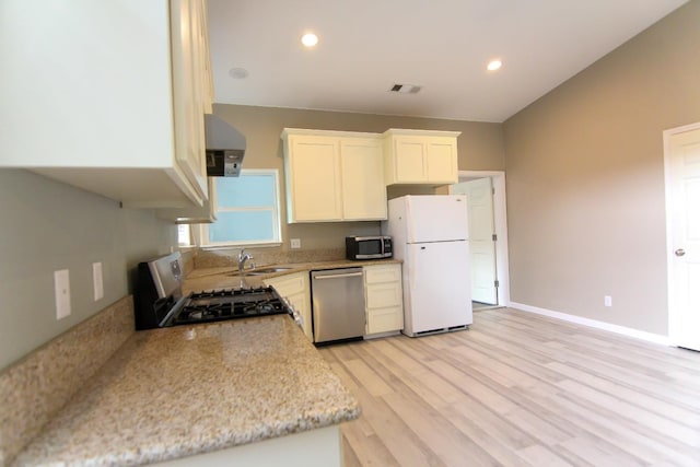 kitchen with appliances with stainless steel finishes, sink, white cabinets, light stone counters, and light wood-type flooring