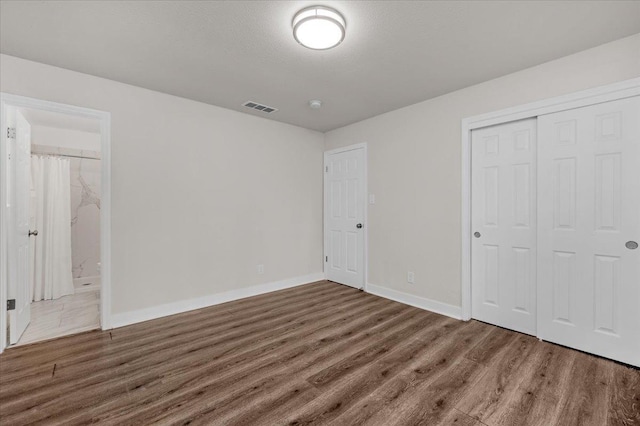 unfurnished bedroom with a textured ceiling, wood finished floors, visible vents, baseboards, and a closet