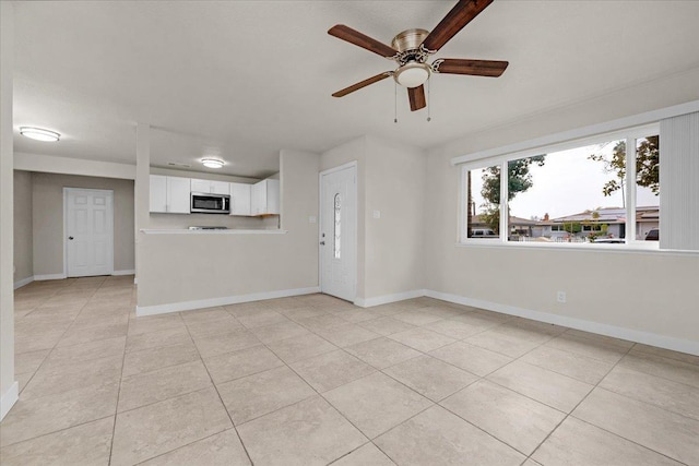 unfurnished living room with light tile patterned flooring, a ceiling fan, and baseboards