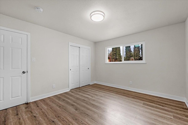 unfurnished bedroom with a closet, a textured ceiling, baseboards, and wood finished floors