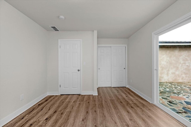 unfurnished bedroom featuring a closet, wood finished floors, visible vents, and baseboards