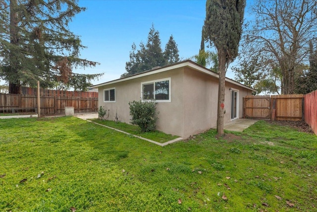 rear view of property with a yard, a fenced backyard, and stucco siding