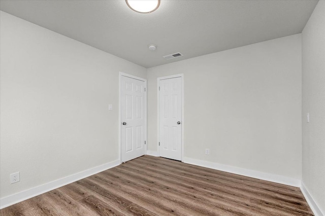 unfurnished room with wood finished floors, visible vents, and baseboards