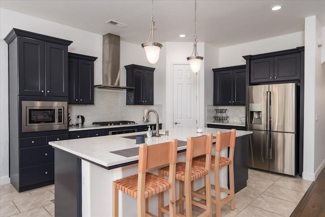 kitchen featuring appliances with stainless steel finishes, decorative light fixtures, a kitchen bar, wall chimney range hood, and a center island with sink