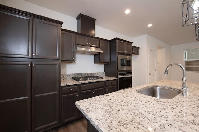 kitchen with sink, light stone counters, dark brown cabinets, hanging light fixtures, and stainless steel appliances