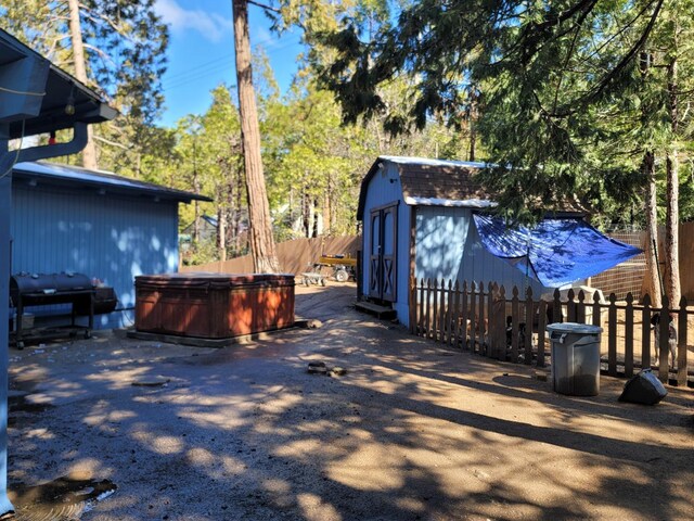 view of property exterior featuring an outbuilding, fence, a shed, a gambrel roof, and a hot tub