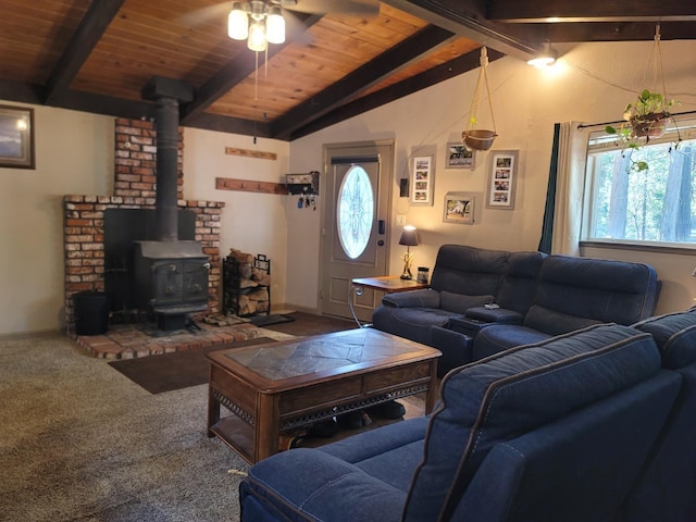 carpeted living area with lofted ceiling with beams, wood ceiling, a wood stove, and a ceiling fan