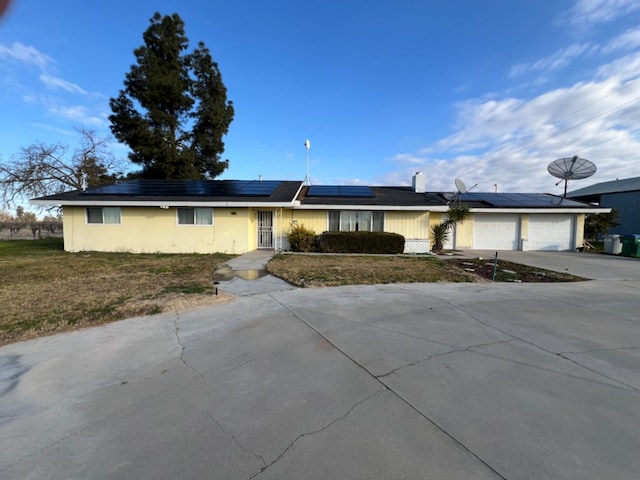 ranch-style home with a garage, a front lawn, and solar panels