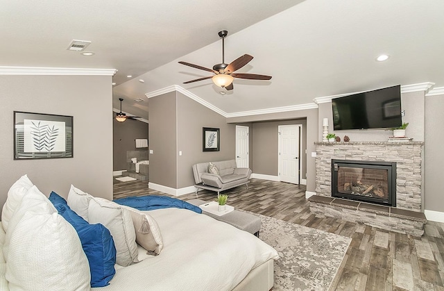 bedroom with vaulted ceiling, a stone fireplace, hardwood / wood-style floors, ceiling fan, and crown molding