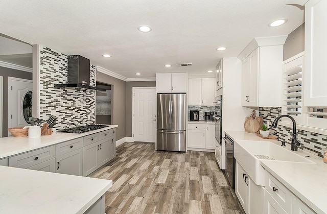 kitchen with wall chimney exhaust hood, crown molding, light hardwood / wood-style flooring, appliances with stainless steel finishes, and white cabinets