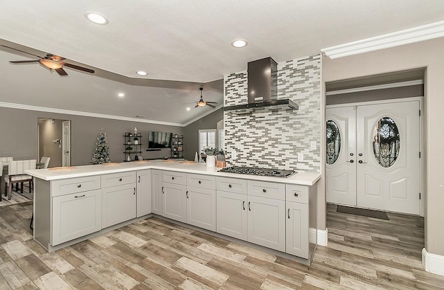 kitchen with white cabinetry, stainless steel gas cooktop, kitchen peninsula, crown molding, and wall chimney exhaust hood