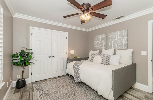 bedroom with hardwood / wood-style flooring, ornamental molding, ceiling fan, and a closet