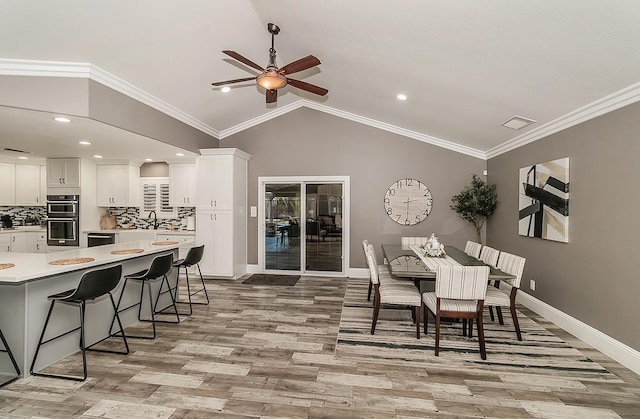 dining space featuring crown molding, vaulted ceiling, ceiling fan, and light wood-type flooring