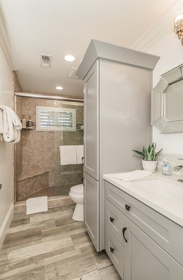 bathroom with hardwood / wood-style floors, ornamental molding, vanity, walk in shower, and toilet