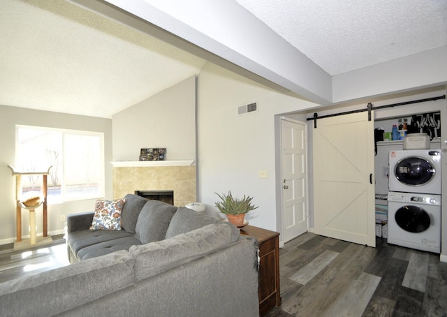 living room with lofted ceiling, dark hardwood / wood-style floors, stacked washer / drying machine, a fireplace, and a barn door