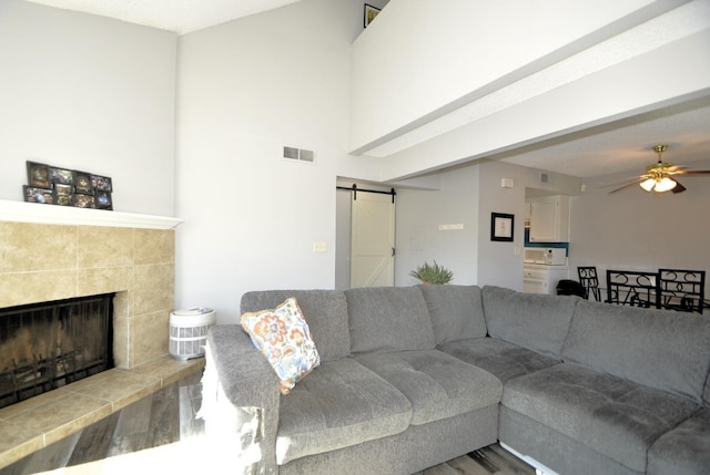 living room with ceiling fan, wood-type flooring, a barn door, and a tile fireplace