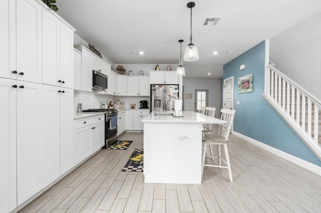 kitchen featuring appliances with stainless steel finishes, pendant lighting, white cabinetry, a kitchen breakfast bar, and a kitchen island with sink