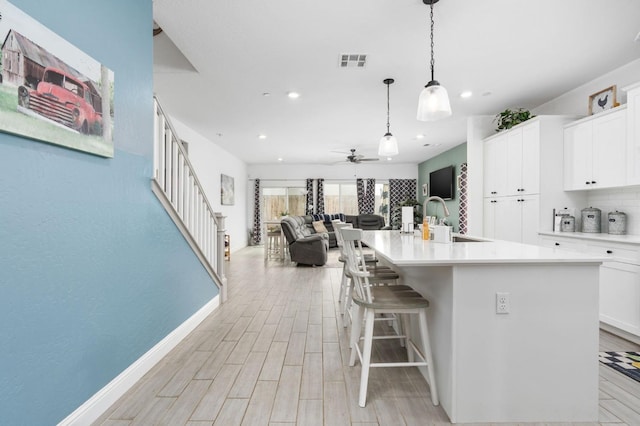 kitchen featuring sink, hanging light fixtures, an island with sink, and white cabinets