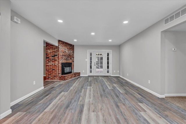 unfurnished living room featuring hardwood / wood-style flooring, a brick fireplace, and french doors