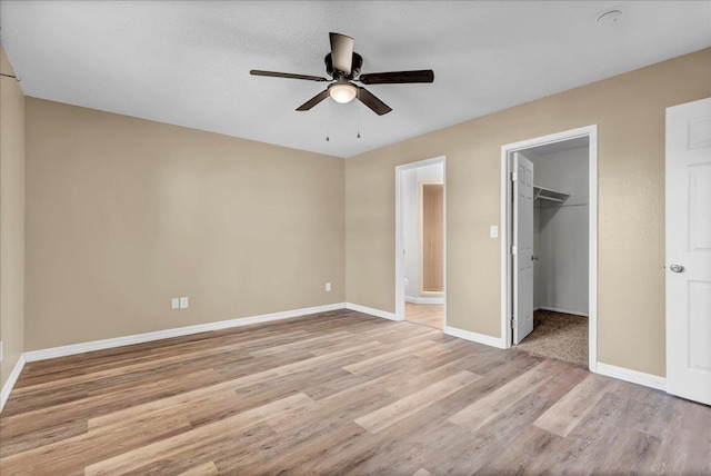 unfurnished bedroom with ensuite bathroom, a walk in closet, ceiling fan, light wood-type flooring, and a closet