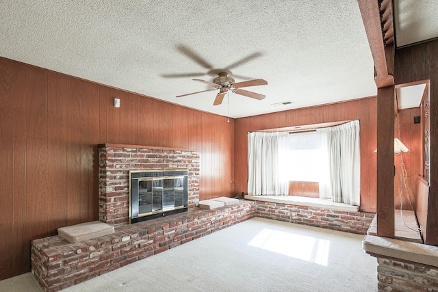 unfurnished living room featuring carpet floors, wooden walls, a textured ceiling, and a fireplace