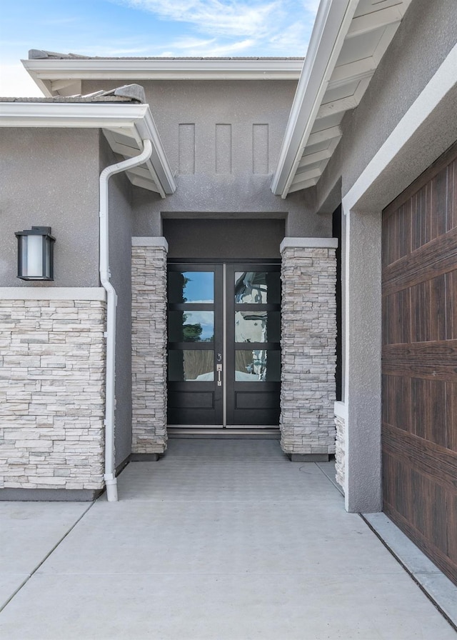 entrance to property with stucco siding, stone siding, and french doors