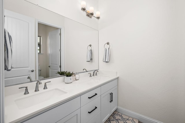 bathroom with baseboards, a sink, double vanity, and toilet