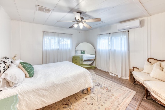 bedroom featuring a ceiling fan, a wall mounted AC, wood finished floors, and visible vents