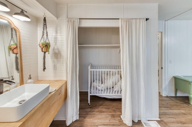 bathroom with wood walls, visible vents, a sink, and wood finished floors