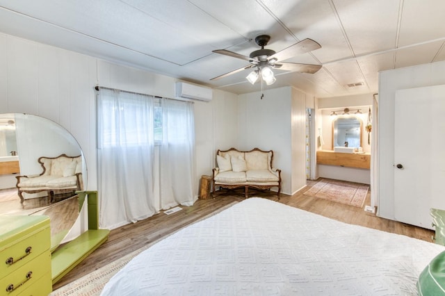 bedroom featuring visible vents, ensuite bathroom, a wall mounted air conditioner, light wood-type flooring, and a ceiling fan