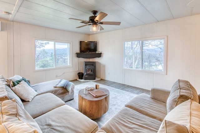 living area with ceiling fan, a wood stove, and wood finished floors