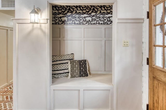 mudroom with wainscoting, brick floor, a decorative wall, and visible vents