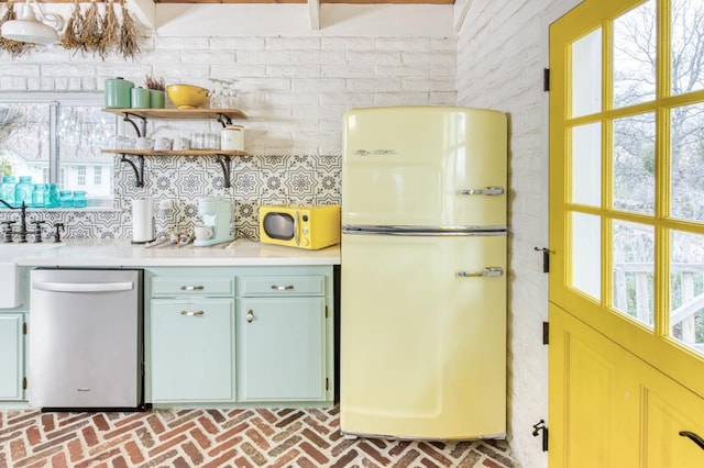 kitchen featuring brick floor, light countertops, freestanding refrigerator, a wealth of natural light, and stainless steel dishwasher