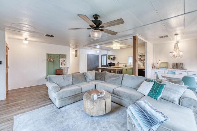 living area featuring visible vents, ceiling fan with notable chandelier, and wood finished floors